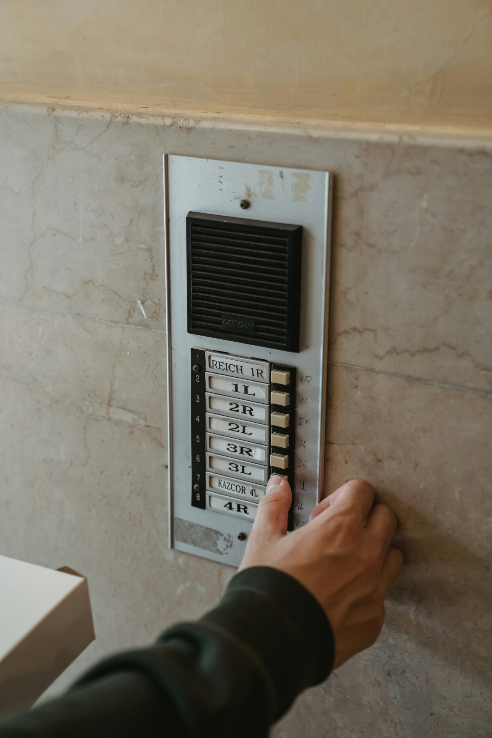Close-up of a hand pressing an intercom button outdoors on a building wall.
